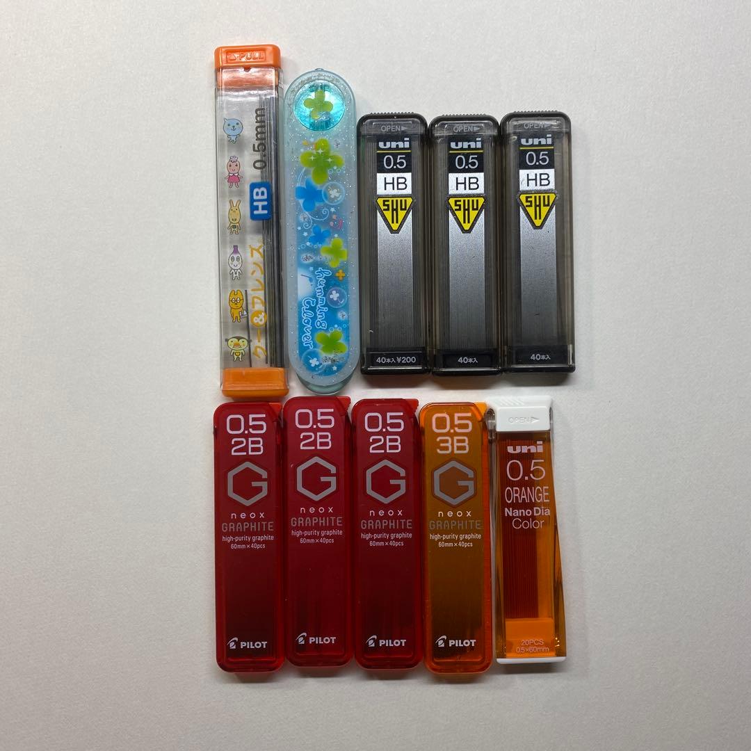 Multiple 0.5mm mechanical pencil refill containers in different colors and brands on a white background.