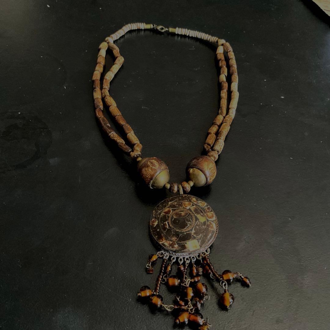 Vintage amber necklace with double-strand beads, a round decorative pendant, and a dangling amber bead tassel on a dark background.