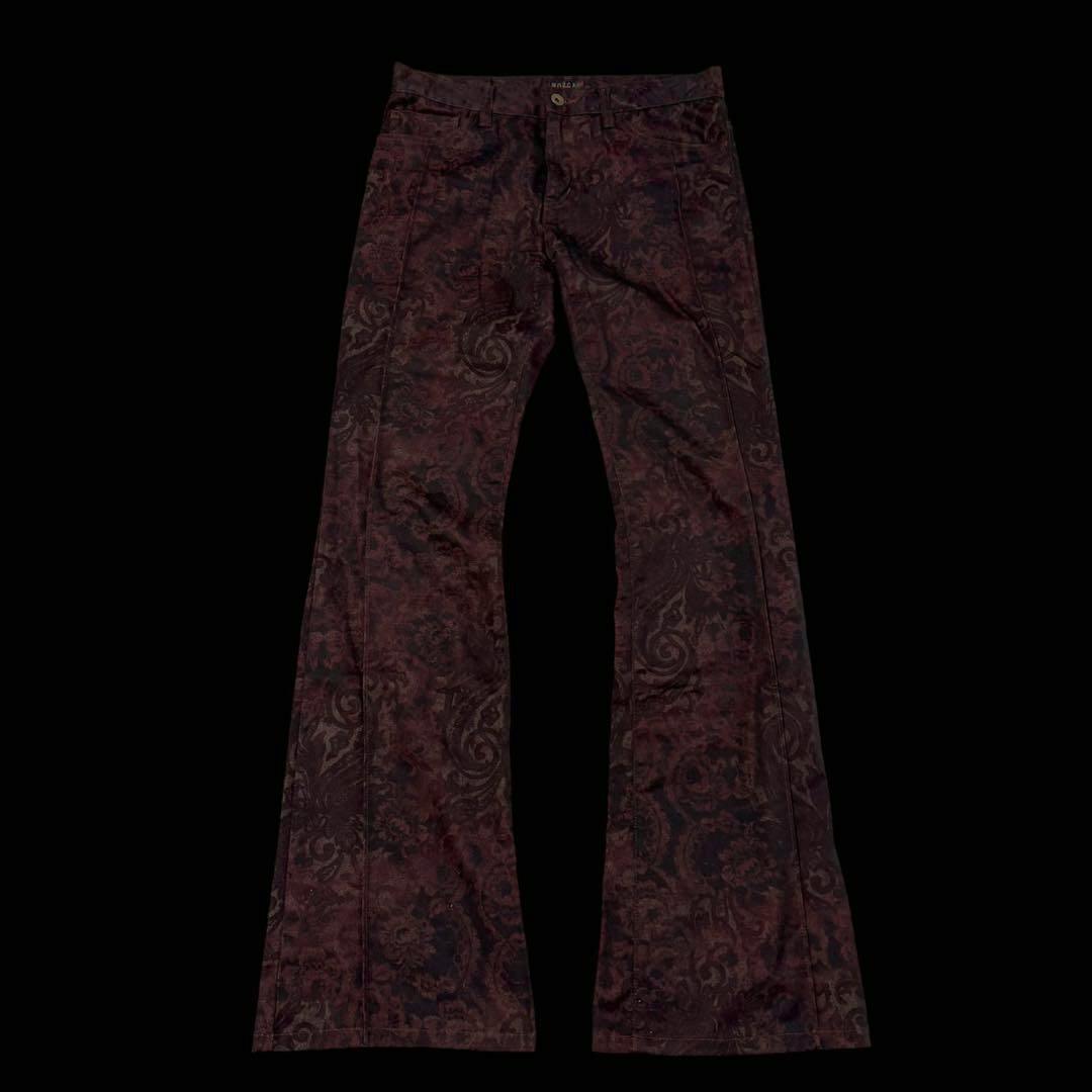 A pair of men's flared pants with a dark ornamental pattern laid flat on a black background.