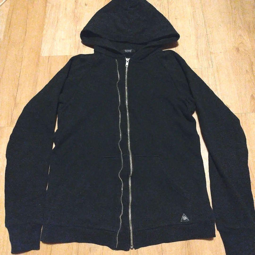 Front view of a black UNDERCOVERISM double-zip hooded sweatshirt laid flat on a wooden floor.