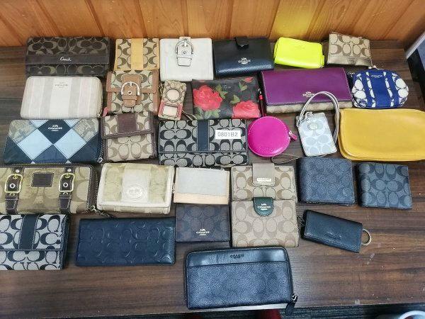 A tabletop arrangement of multiple used Coach wallets, coin purses, and key cases in various colors and patterns.