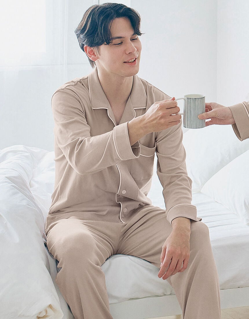 A man wearing the cotton pajama set is sitting on a bed while receiving a cup.