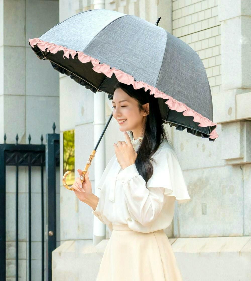 Woman holding the 100%遮光日傘 with a gray canopy and pink ruffled edge.
