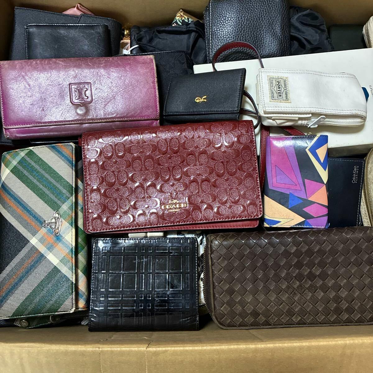 Cardboard box filled with assorted wallets, including a red Coach wallet and a green plaid Vivienne Westwood wallet.