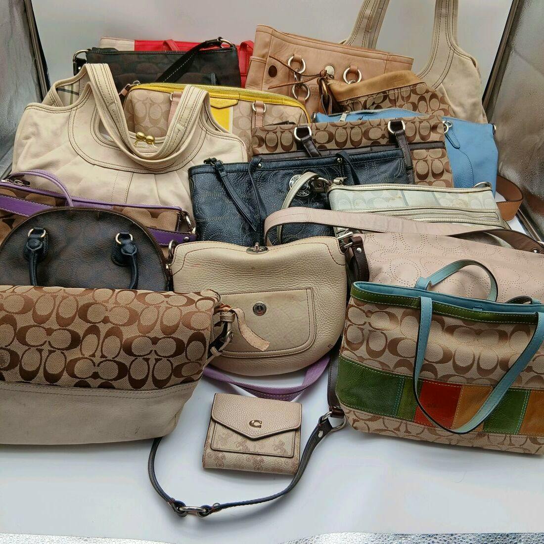 Several Coach bags and a small Coach wallet arranged together on a white surface, many showing the signature 'C' canvas pattern.