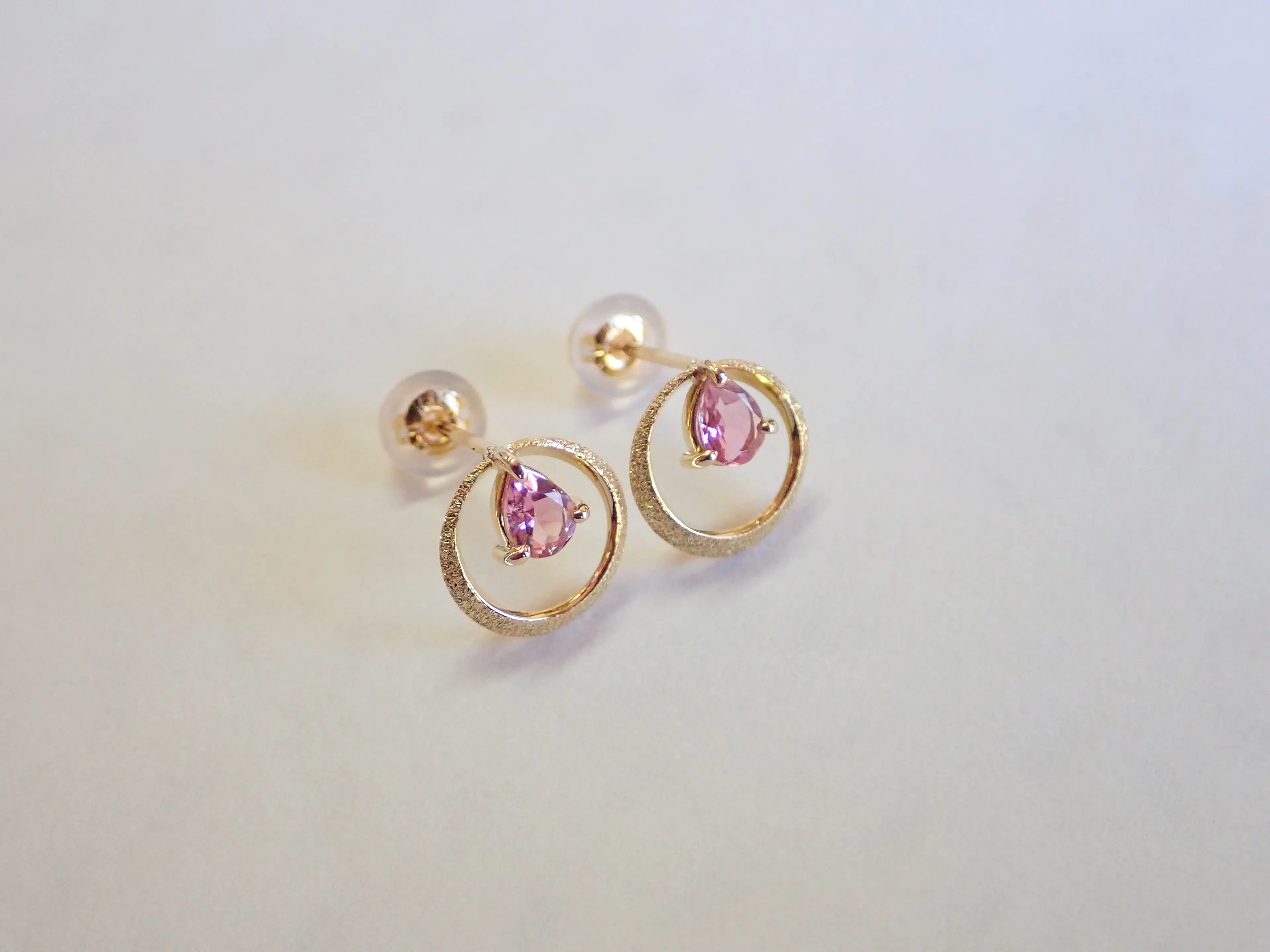 Close-up photo of a pair of pink tourmaline pear-shaped moon earrings in yellow gold on a white background.