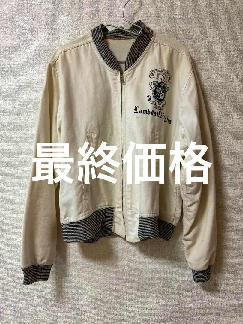Front view of a cream cotton men's jacket with a zipper and a Lambda Chi Alpha crest, hanging on a wall.