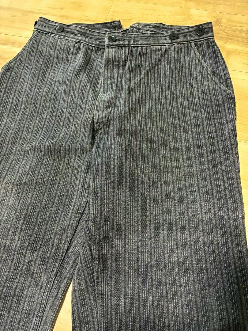 A pair of men's cotton pants with vertical stripes laid flat on a wooden floor, showing the front and waistband.