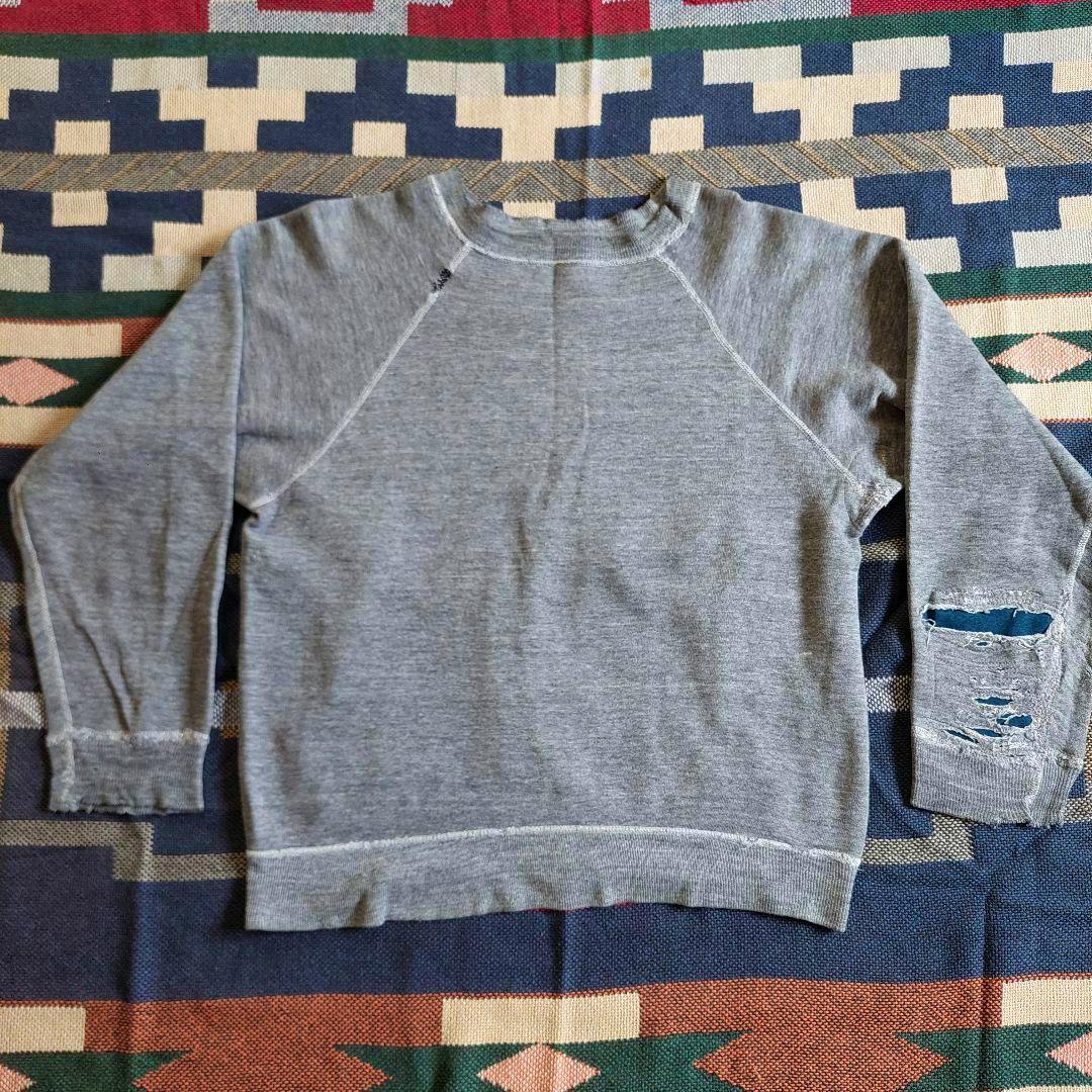 Gray cotton sweatshirt laid flat showing long raglan sleeves and distressed holes on the right sleeve.