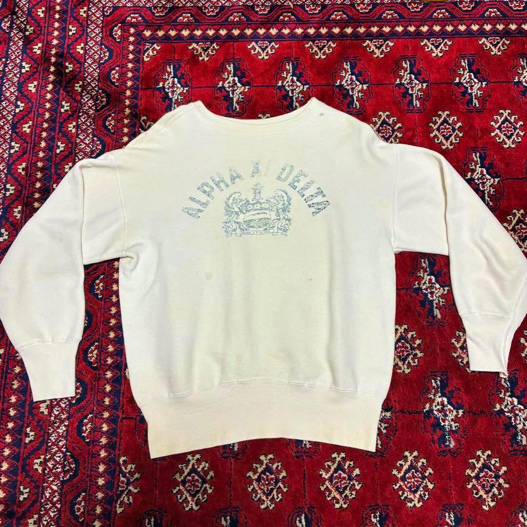 50s vintage cotton sweatshirt laid flat showing the back with faded "ALPHA XI DELTA" text and crest on a red patterned rug.