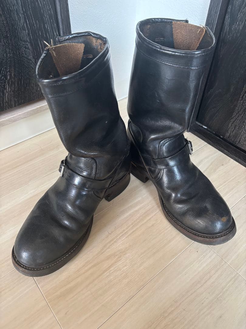 Pair of leather engineer boots with ankle straps and buckles photographed on a light wood floor.