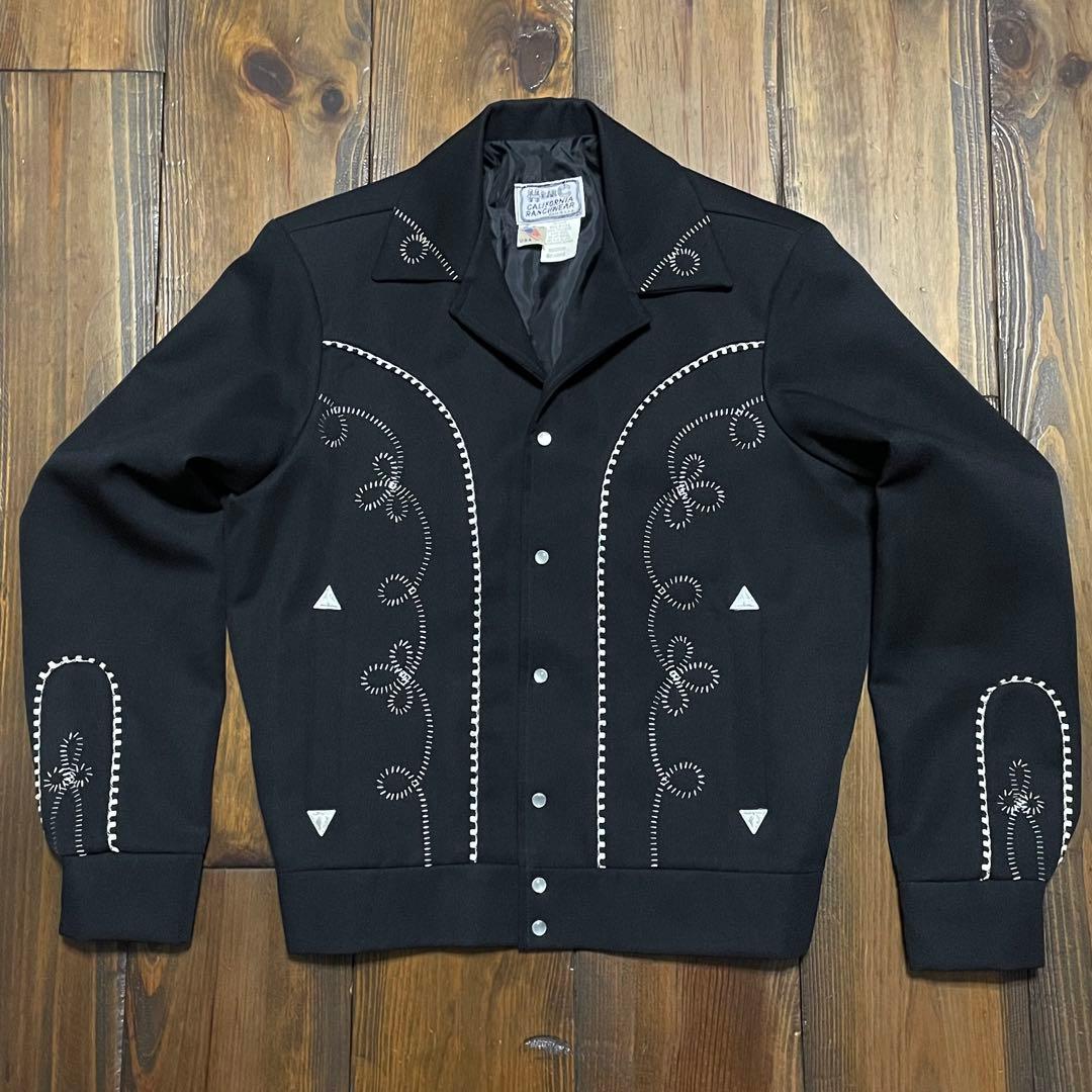 Black 60s H Bar C western men's polyester jacket with white decorative stitching and snap buttons laid flat on a wooden floor.