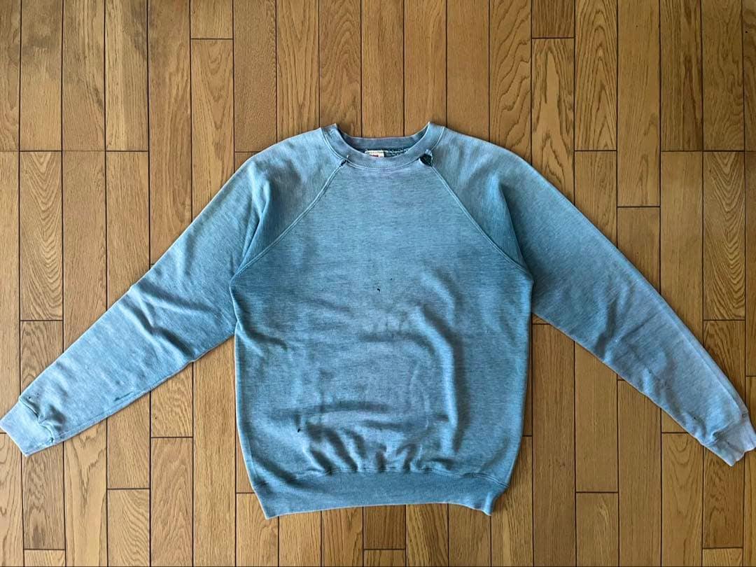 Faded green men's cotton shirt laid flat on a wooden floor showing the front and sleeves.