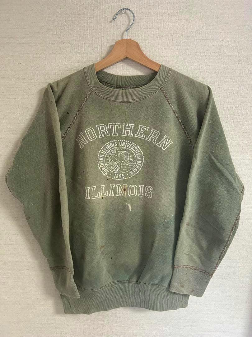 Front view of a green vintage college sweatshirt with "NORTHERN ILLINOIS" print hanging on a wooden hanger against a wall.