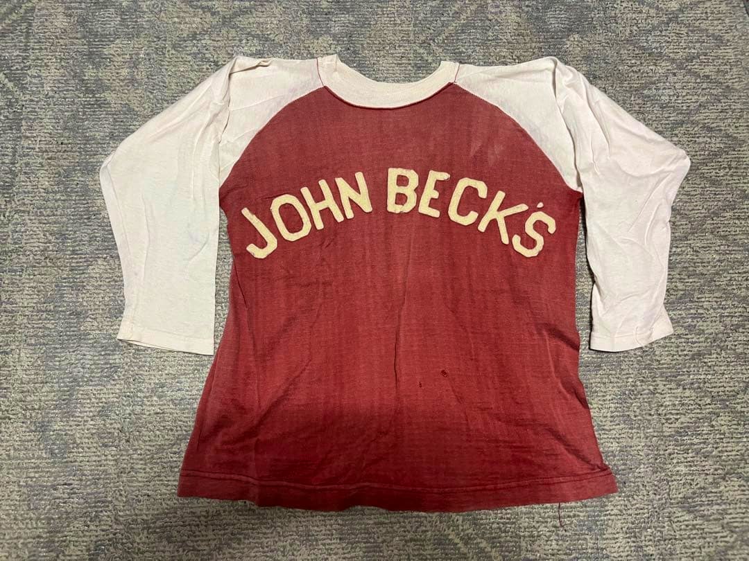 Red raglan cotton T-shirt with white sleeves and "JOHN BECK'S" lettering across the front.