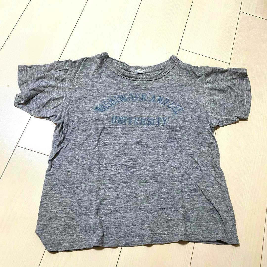 Gray children's Champion T-shirt laid flat on a light wood floor showing the faint front printed text.