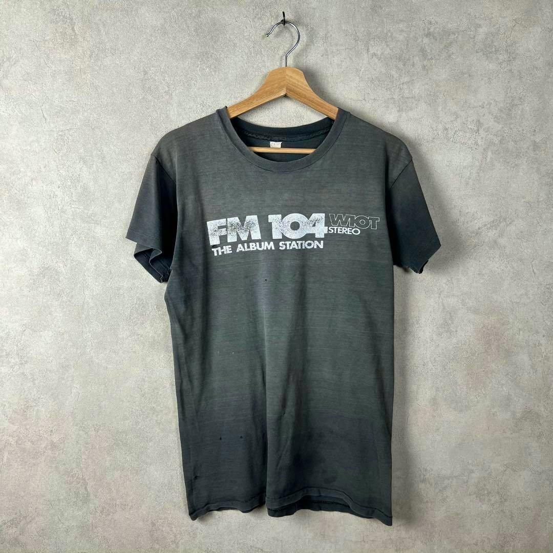Front view of a vintage black men's cotton T-shirt with 'FM 104 THE ALBUM STATION' print hanging on a wooden hanger.