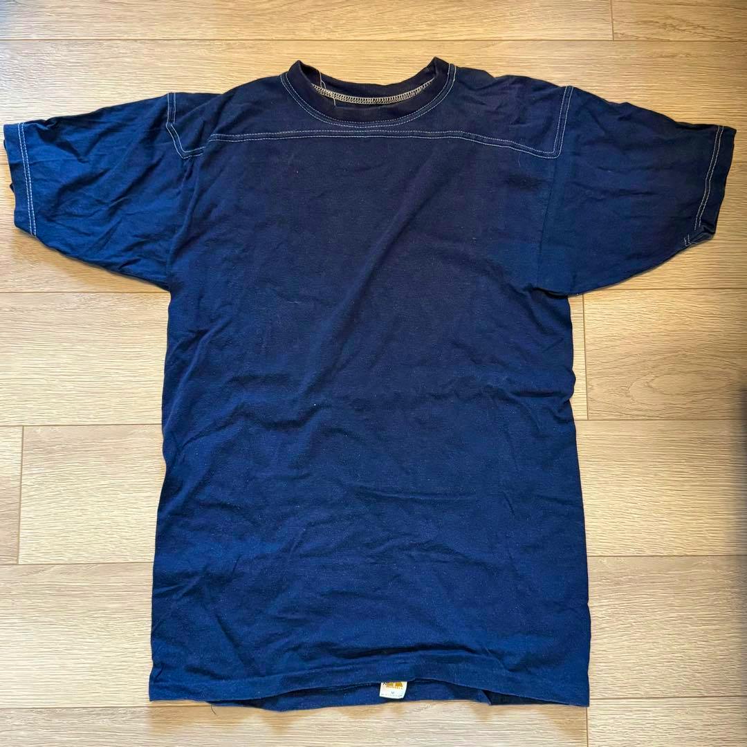 Flat-lay photo of the Russell men's cotton T-shirt (front) in dark blue with contrast topstitching and a visible gold tag at the hem.