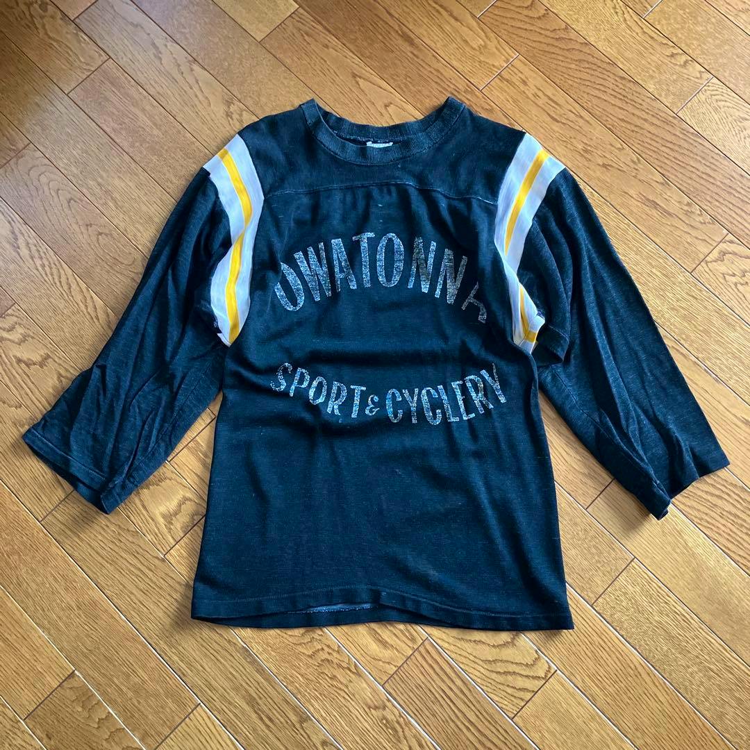 70's vintage black men's three-quarter sleeve cotton T-shirt laid flat, showing white and yellow shoulder stripes and distressed printed text.