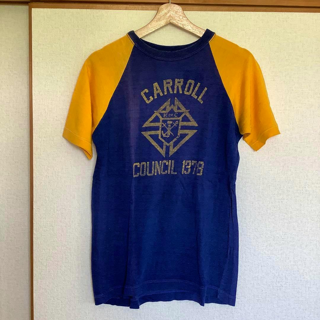 Blue body with yellow raglan sleeves men's T-shirt printed "CARROLL COUNCIL 1378" hanging on a hanger against a wall.