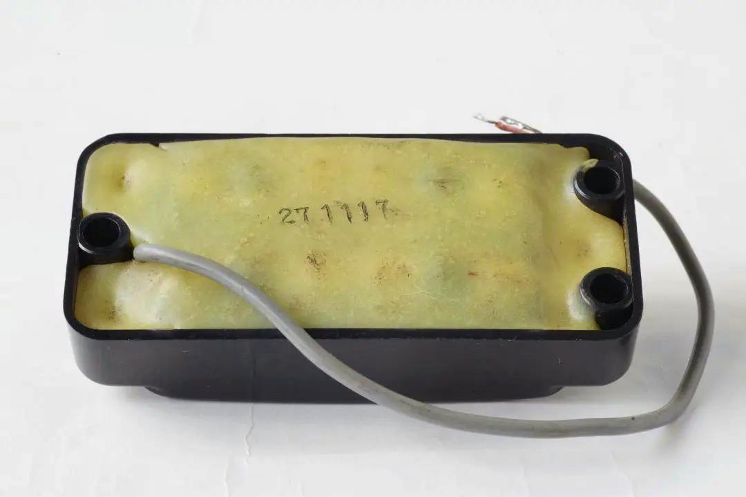 Bottom view of a rectangular guitar pickup showing yellowed potting compound, a black plastic housing, and a gray lead wire.