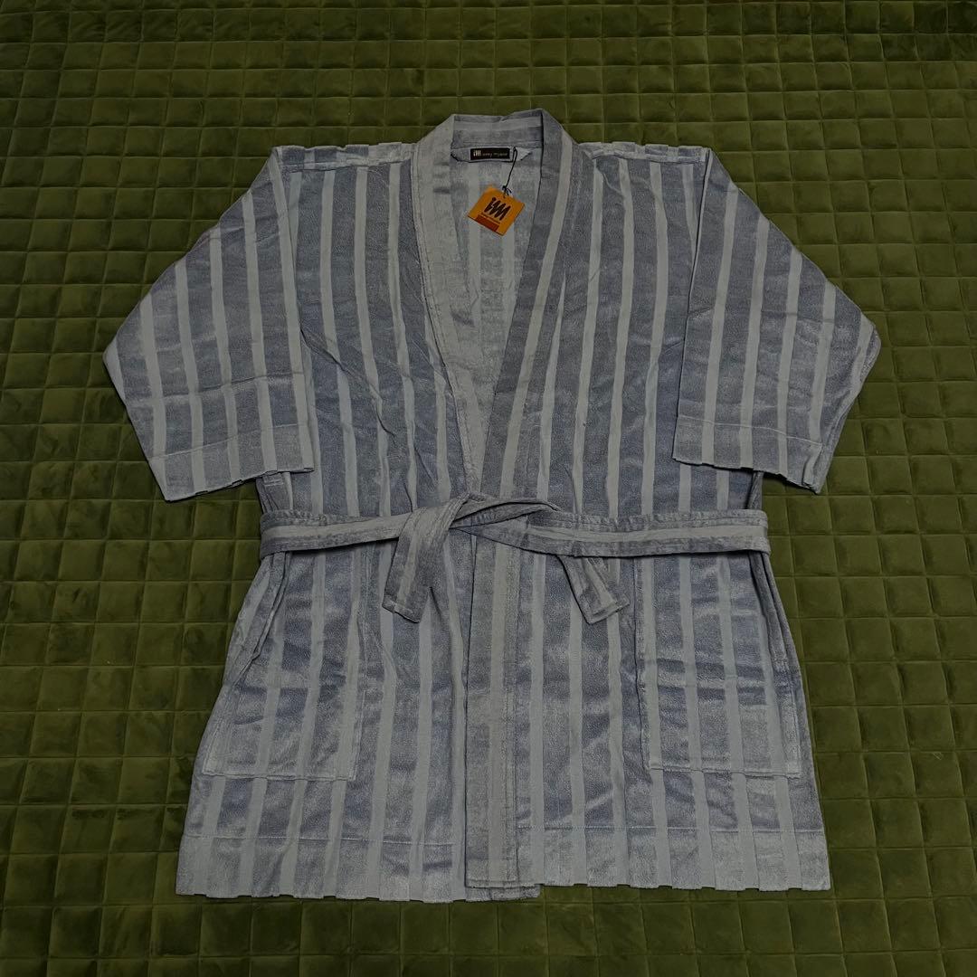 Short Issey Miyake cotton bath robe with belt laid flat on a green quilted surface.