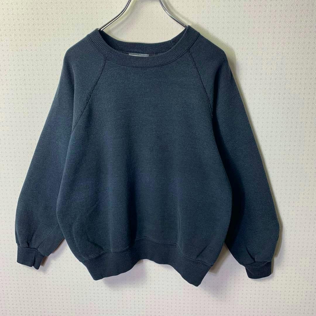 Front view of a black raglan sweatshirt (80s, made in USA, size L) hanging on a hanger against a light wall.