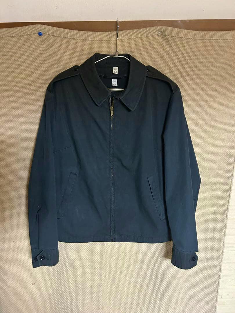 Front view of the black 385 utility men's jacket hanging on a hanger against a beige background.
