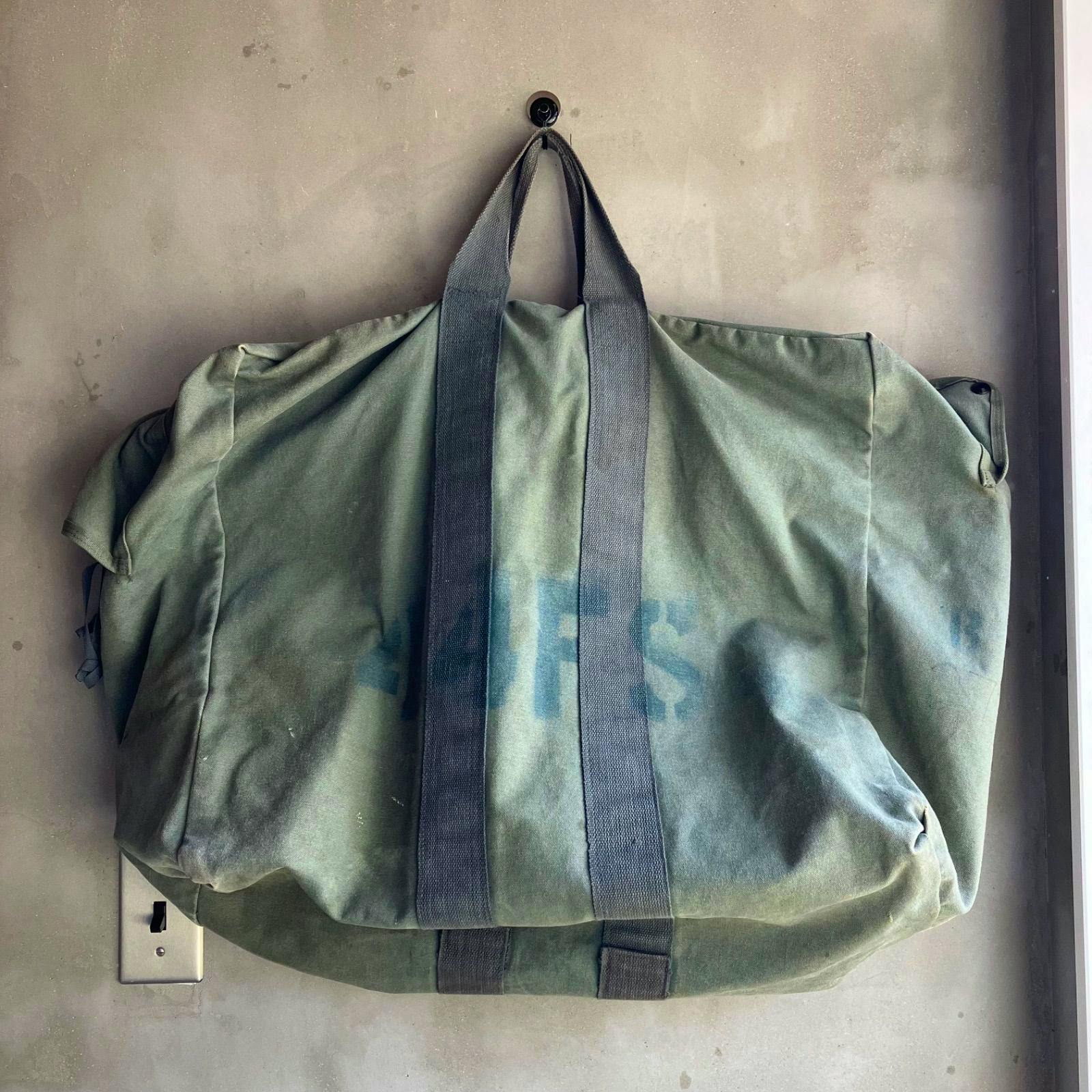 Green cotton canvas USAF-style duffel/boston bag hanging showing top handles and front panel.