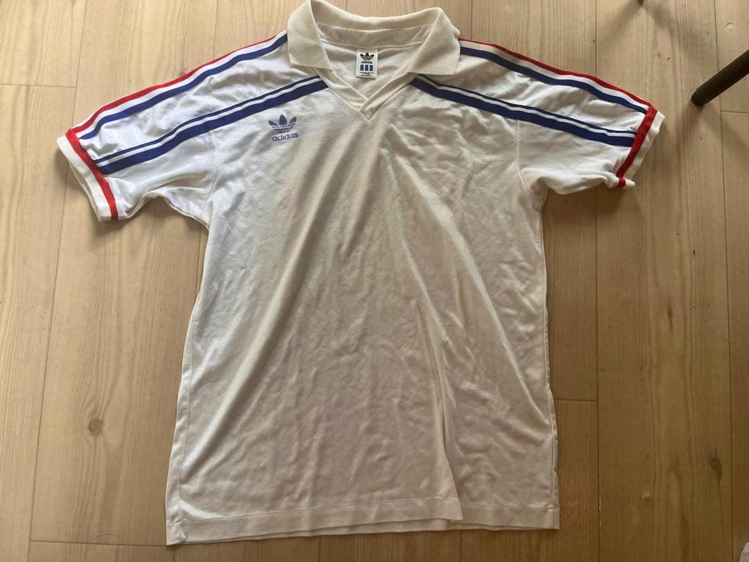 Front view of the white 1986 France adidas football jersey laid flat, showing the trefoil logo and blue and red shoulder stripes.