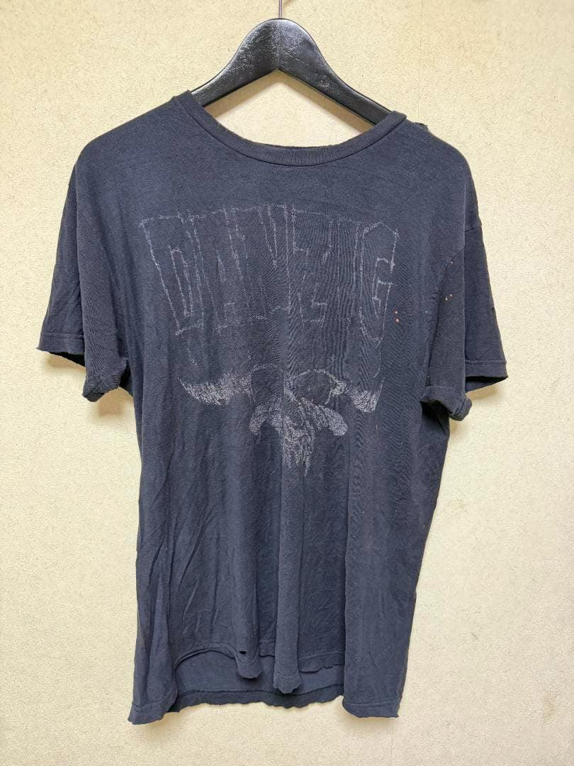 Faded front view of a black 90s Danzig cotton T-shirt hanging on a hanger, showing worn graphic and distressing.