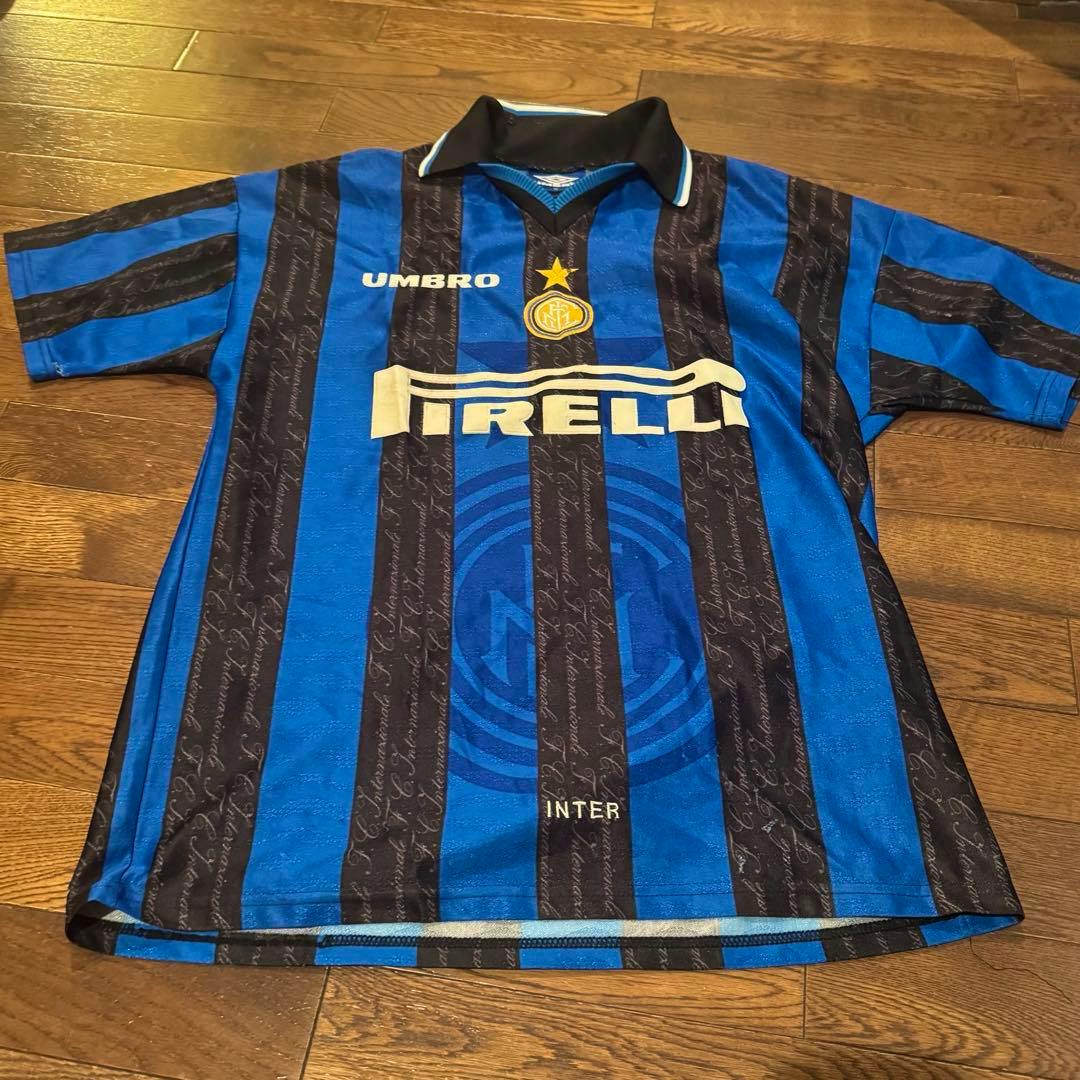 Blue and black striped Inter Umbro jersey with Pirelli sponsor laid flat on a wooden floor.