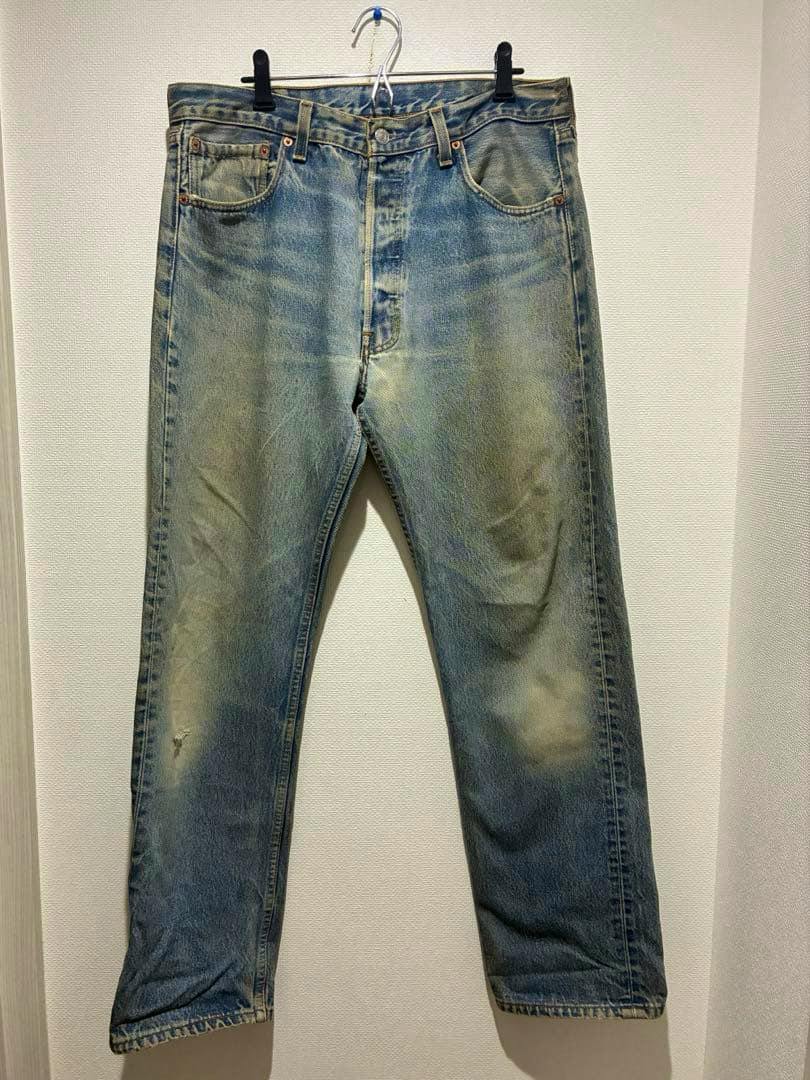 Front view of men's Levi's 501XX denim jeans hanging on a hanger against a white wall.