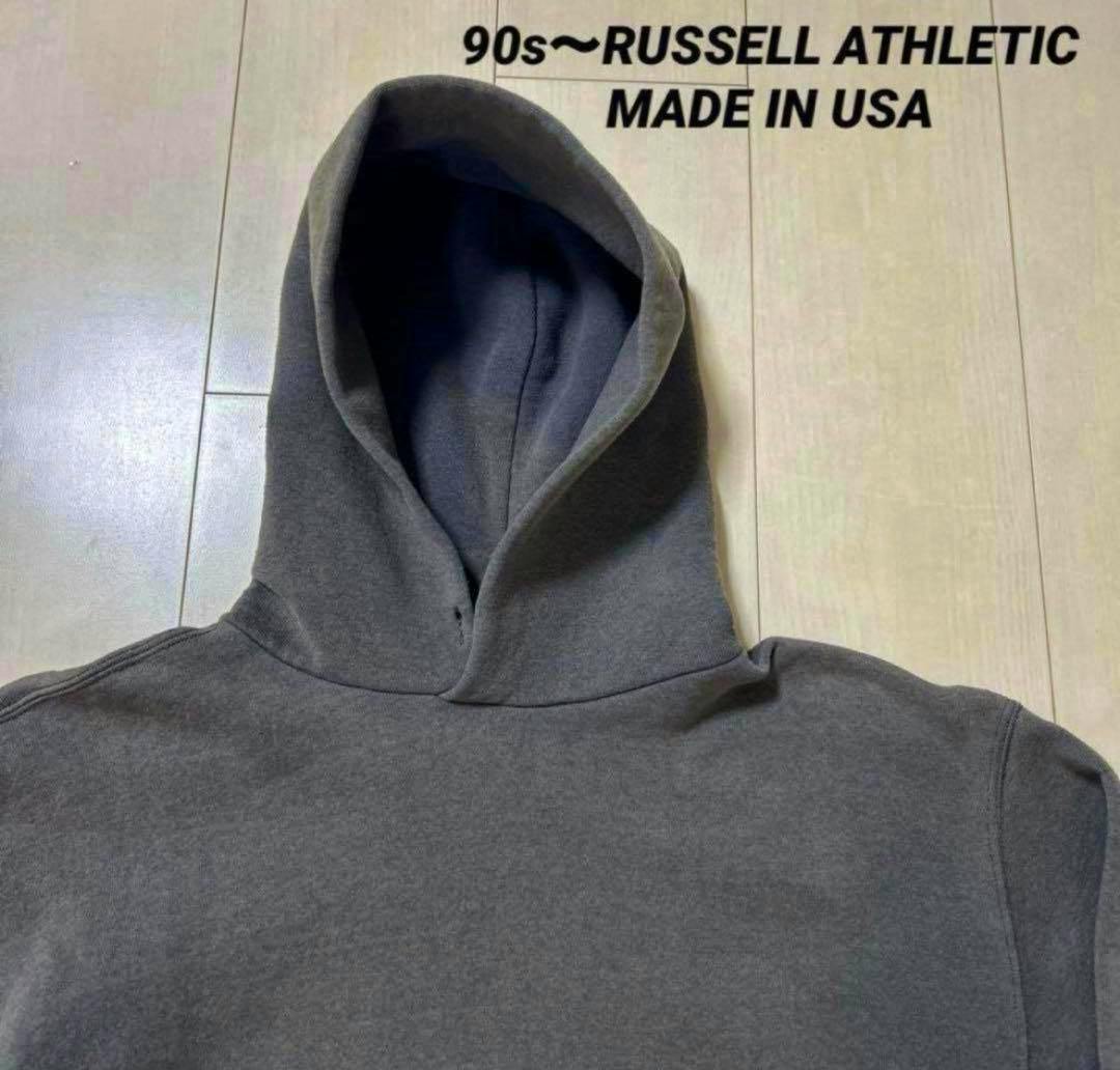 Gray hooded Russell Athletic 90s-era sweatshirt laid flat on a wooden floor.