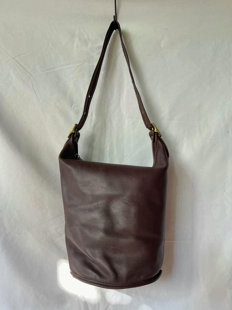 Brown bucket-style shoulder bag with a single adjustable strap hanging against a white background.