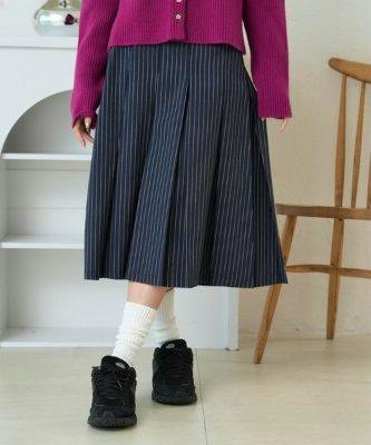 Front view of a model wearing a dark pinstripe midi pleated skirt paired with white socks and black sneakers.