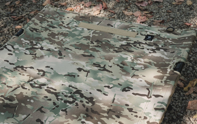 Camouflage fabric surface of the 2WAY TACTICAL COT showing seams, corner buckles, and a small tag.