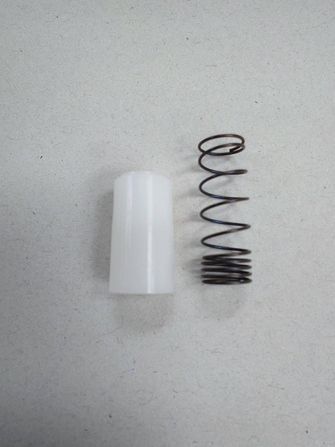 A white cylindrical spacer and a metal coil spring for a small joystick shown side by side on a neutral background.