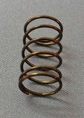 A small metal coil spring for a joystick standing upright on a gray fabric surface.