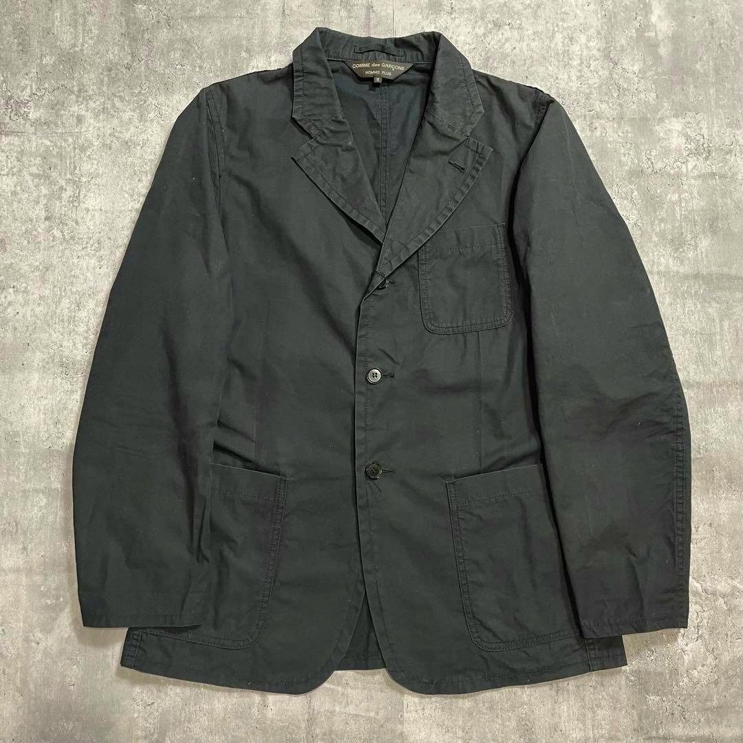 Black Comme des Garçons Homme Plus tailored cotton men's jacket laid flat showing the front, lapels, buttons, and patch pockets.