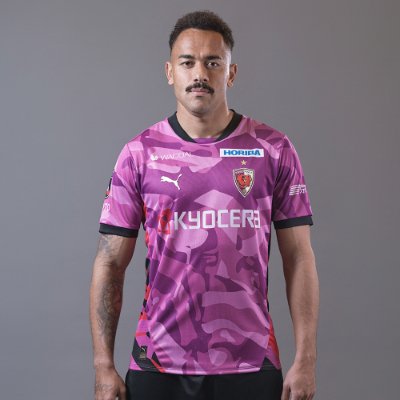 Front view of the 2026 百年構想リーグオーセンティックユニフォーム 1st worn by a person; purple camouflage jersey with sponsor logos on chest and shoulders.