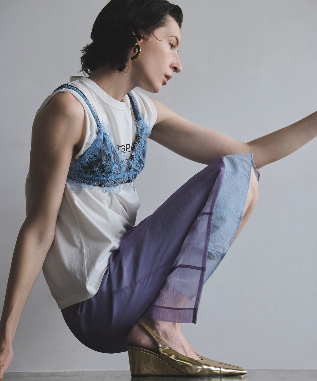 A crouching model wearing the sheer layered color skirt in purple paired with a white top and blue lace overlay.
