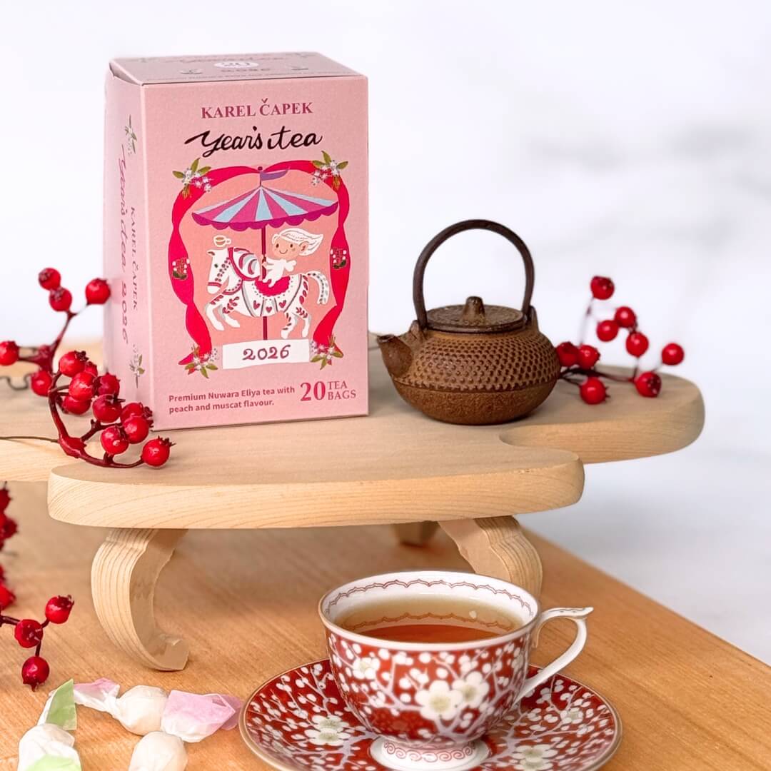 A pink 2026 tea box for black tea bags displayed on wooden stands beside a small teapot, a cup of brewed tea, and decorative red berries.