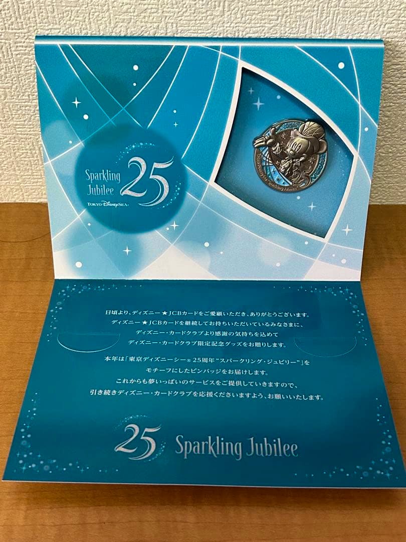 A blue Sparkling Jubilee 25 Tokyo DisneySea presentation card with a Mickey pin badge displayed in a cutout window.