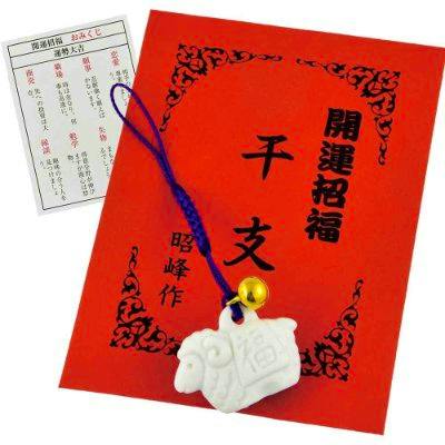 White sheep charm with a purple cord and small bell displayed on a red backing card with Japanese text and a small paper fortune slip.