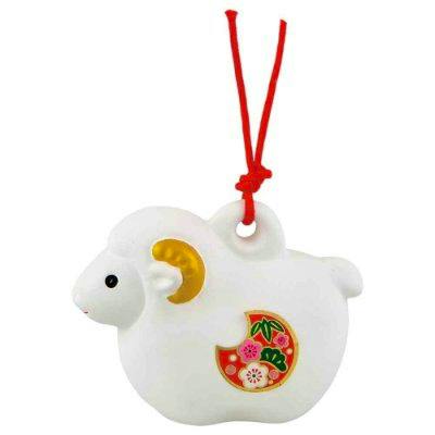 White sheep-shaped plastic charm with a red hanging cord, gold-painted horn, and a decorative floral motif on its side.
