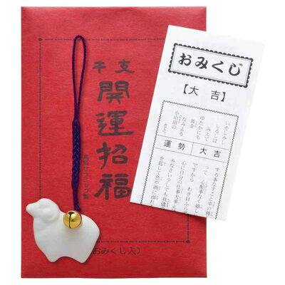 White sheep-shaped plastic charm on a purple cord with a small gold bell, shown on red backing alongside a folded omikuji paper.