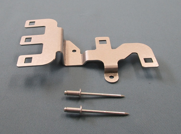 Metal mounting bracket and two blind rivets photographed on a gray surface.