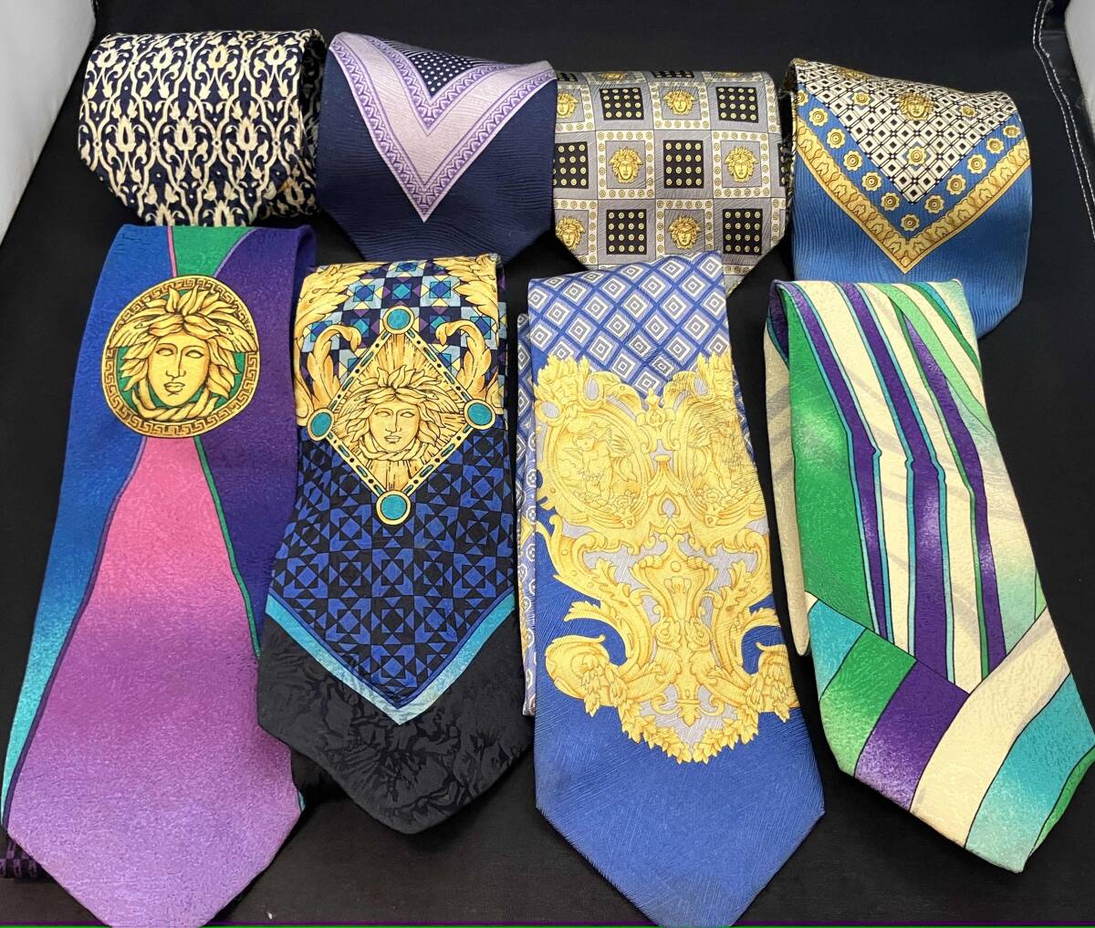 Several silk neckties arranged in two rows showing various colorful patterns and medallion motifs.