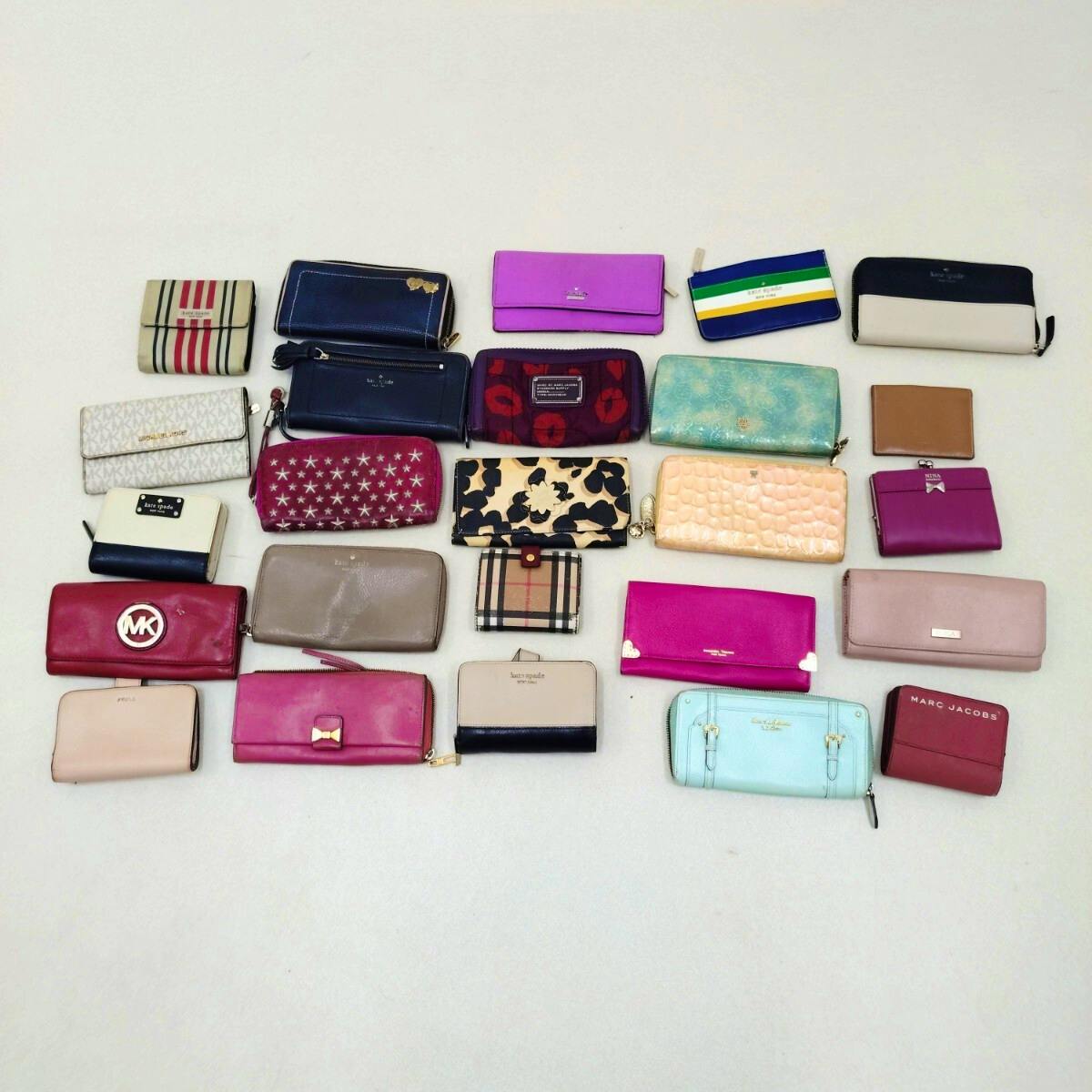A laid-out assortment of 25 branded wallets and small purses arranged on a light background.